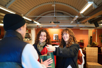 Male owner giving shopping bag to female customer at checkout counter in clothing store