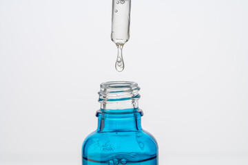 Dropper with a drop of hyaluronic acid and collagen serum and a blue bottle on a white background. Close-up. Copyspace.