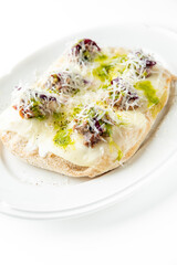 A crispy flatbread topped with melted cheese, shredded vegetables, and herbs, served on a white oval plate. Garnished with grated cheese and a drizzle of green sauce, creating a appetizing dish.