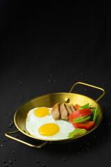 Fried eggs with sausages and vegetables in pan.