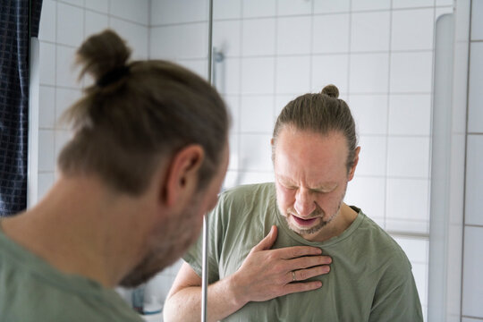 Reflection of man going through chest pain while standing in front of mirror in bathroom