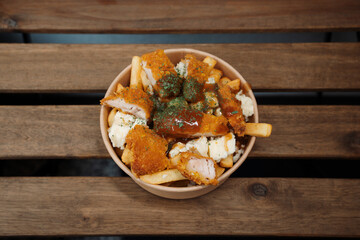 Poutine fries with chees and fried chicken in paper takeout container. Delicious freshly prepared meal, perfect for menus, restaurants, or food delivery concepts.