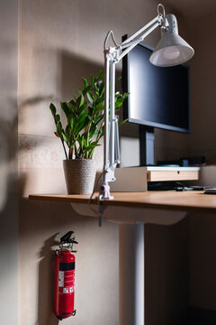 Fire extinguisher mounted on wall under desk with electric lamp and desktop PC