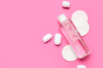 Bottle of micellar water with cotton balls and pads on pink background