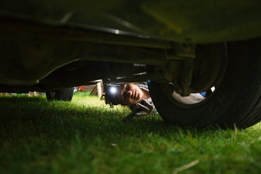 Female mechanic wearing headlamp repairing tire of car while lying down