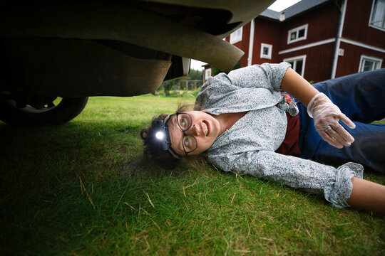Female mechanic wearing headlamp lying down while examining undercarriage of car