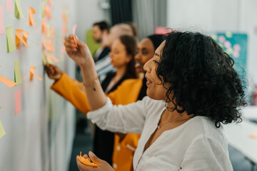 Smiling curly haired businesswoman sticking adhesive note on whiteboard in office