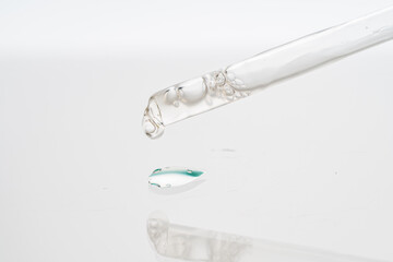 Dropper with collagen and hyaluronic acid serum on a white background with reflection. A drop of lotion for the skin of the face on the glass. Close-up, macro photography. Space for text