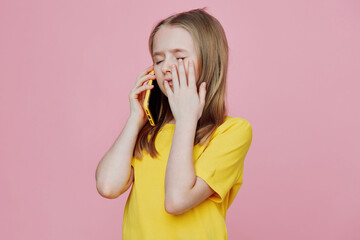 Young girl expressing emotion while talking on the phone, wearing a bright yellow t shirt against a...