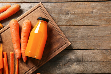 Board with bottle of fresh carrot juice on wooden background
