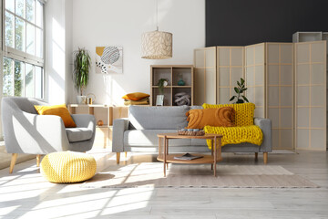 Interior of light living room with  grey sofa, armchair and wooden coffee table