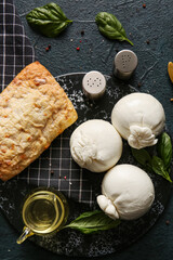 Board of tasty Burrata cheese with basil and bread on dark background