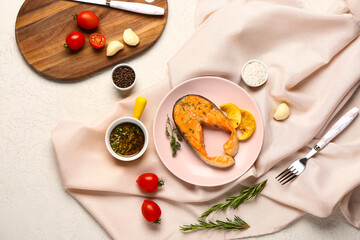 Plate of tasty salmon steak with tomatoes, sauce, garlic and lemon on white background
