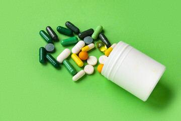 Jar with different scattered pills on green background