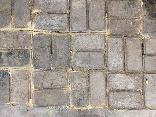 Close-up, top-down view of a paved surface made of rectangular and square grey interlocking pavers. Joints between the pavers are visible, filled with grit. They exhibit signs of wear and varying tone
