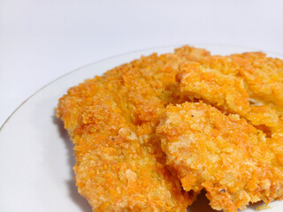Multiple pieces of deep-fried chicken, each coated in a crispy, textured breading that gives it a vibrant golden-orange hue, are arranged on a round white plate. The breading appears flaky and crunchy
