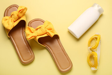 Female stylish flip flops with sunscreen cream and goggles on yellow background