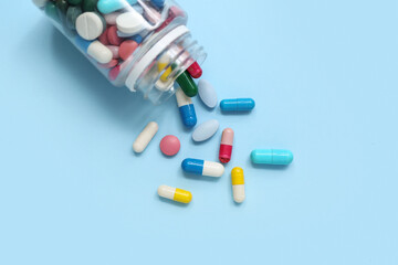 Overturned bottle with different pills on color background
