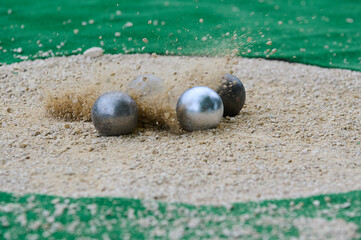 Petanque precision shooting competition moment with metal balls hitting target in sand, dust flying on impact. Focus on accuracy and dynamic play