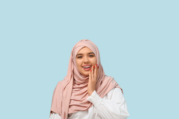 Fototapeta premium Happy young Muslim woman in hijab on blue background