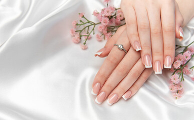 Woman showing french manicure and engagement ring on white satin background