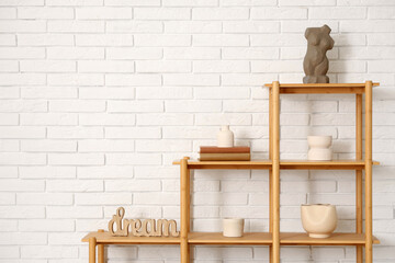 Wooden shelf unit with books and decor near white brick wall