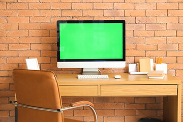 Modern workplace with computer near brick wall in room