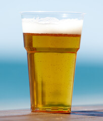 A plastic cup filled with beer is sitting on a wooden table