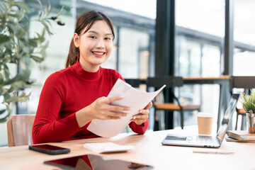 Shot of an attractive businesswoman in red sweater holding papaerwork sitting at her desk in an office.