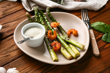 Plate with fried green asparagus and tasty shrimps on wooden background, closeup