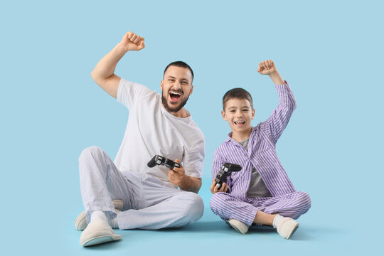 Happy father with his son in pajamas playing video games on blue background