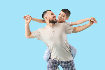 Happy father with his son in pajamas having fun on blue background