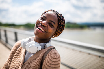 Happy young black woman is looking at camera and smiling. She is enjoying sunny day outdoor.
