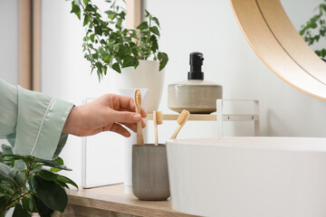 Young woman taking toothbrush from holder near sink in bathroom, closeup