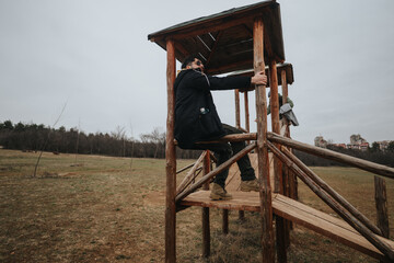 A person in casual attire climbing a wooden structure located in a grassy field, surrounded by an...