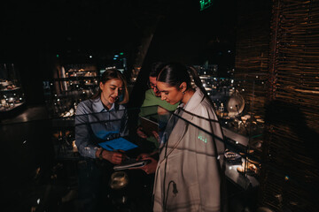 Three people collaborate, referring to digital and physical materials, within a low-lit exhibit...
