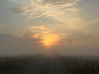 sunrise over the road with wind turbine in the morning fog