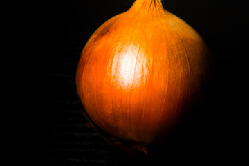 A single, radiant brown onion is spotlighted against a dramatic dark background, highlighting its...