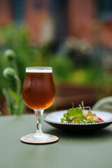 A glass filled with beer and a plate of salad next to it