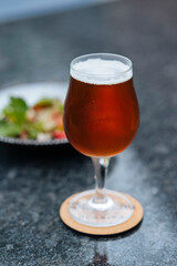 A glass filled with beer and a plate of salad next to it