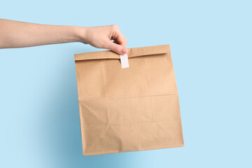 Female hand with paper bag on blue background. Food delivery service
