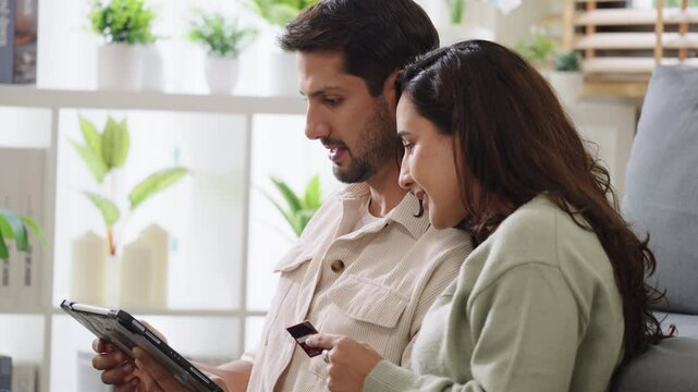 Couple using tablet and credit card to shop online through e-commerce app, making payment and browsing modern platform with promo codes and discount offers