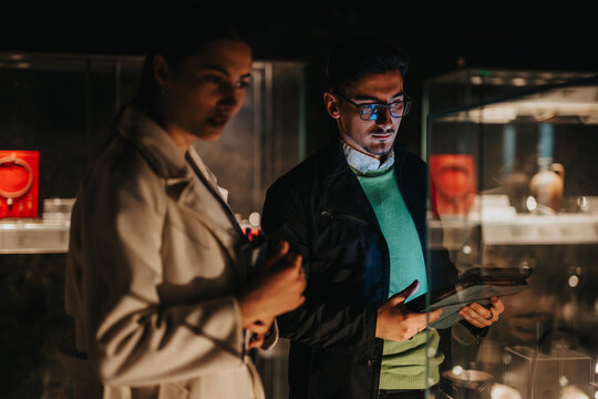 Two people attentively examine displayed artifacts in a dimly lit museum, evoking curiosity and a deep appreciation for art and history.