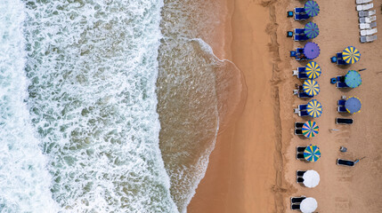 Aerial drone top-down view of the sea waves hitting the beach, tourists play in the sea and...