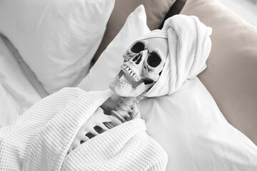 Human skeleton with towel and bathrobe lying in bedroom
