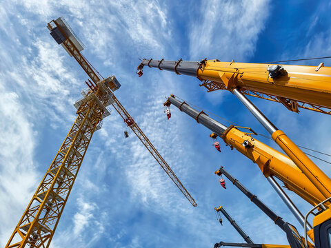 Construction cranes stand tall against a bright blue sky at a busy construction site in a city during midday