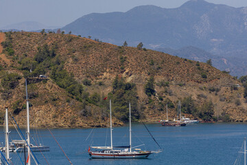 Several yachts anchored in the blue waters of the Gulf of Fethiye near Karagözler Peninsula with mountains in haze. Sunny day. Fethiye, Turkey, Mediterranean.
