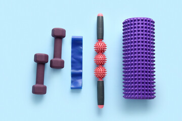 Foam roller with massager, dumbbells and stretching band on blue background