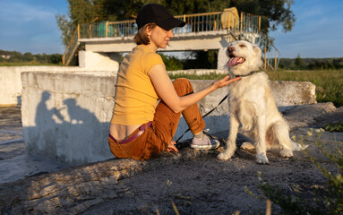 adult girl sitting next to happy dog on walk in park. joy of communication with four-legged friend....