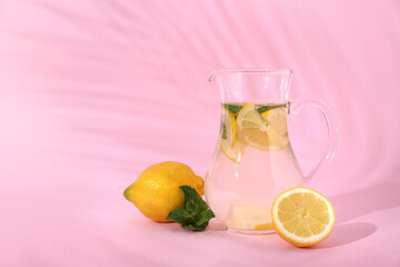 Jug of fresh lemonade with mint and lemons on pink background